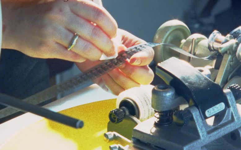 A filmmaker carefully cleans and inspects an 8mm film strip on a film editing viewer