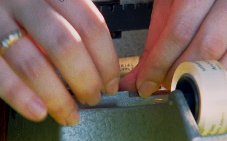 A close-up shot of a person's hands carefully splicing together a strip of film on a vintage tape splicer