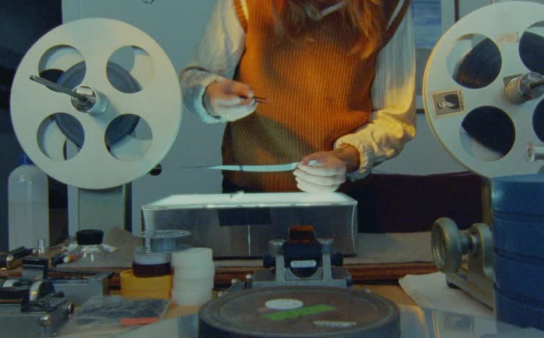 A film editor carefully examines and prepares to splice a strip of analog film over a lightbox in a retro workshop