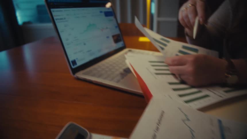 Two business partners analyze financial data, comparing portfolio growth charts on paper with live market trends on a laptop