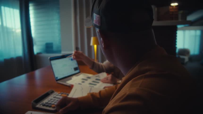 A couple sits at their dining table at night, seriously discussing their finances while looking at charts on a laptop