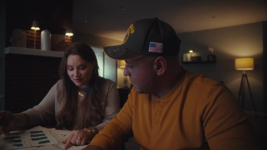 A military veteran and his wife sit at their dining table at night, carefully planning their finances together