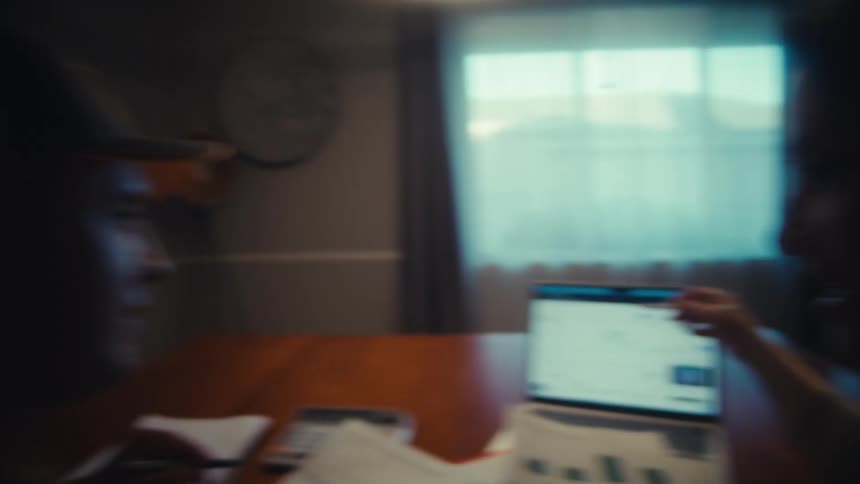 A happy couple reviews their financial charts and data on a laptop and paper documents while working together from home