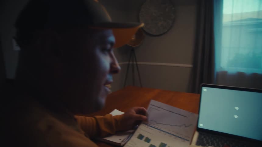 A man and woman review financial data and charts while looking at a laptop with a green screen at their home office table