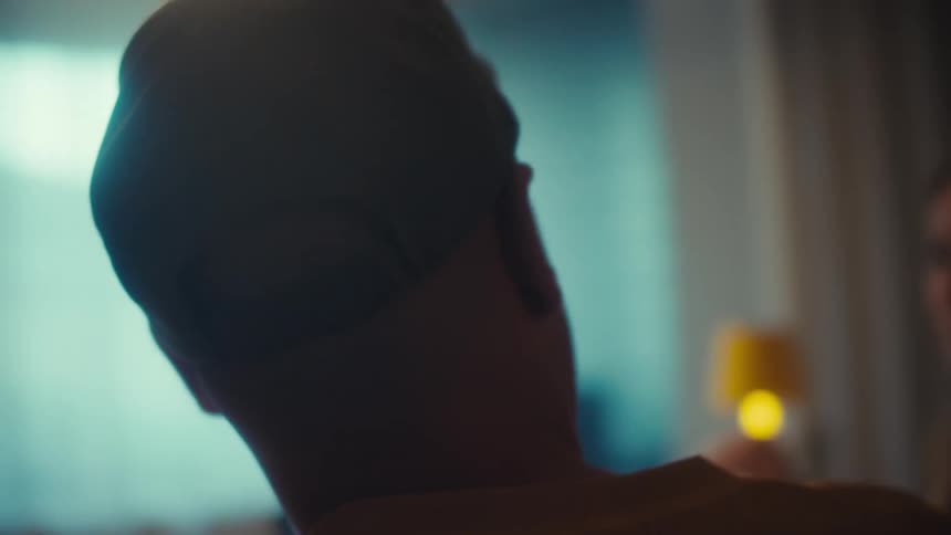 Cinematic slow-motion close-up of a man in a yellow shirt and a baseball cap with an American flag patch smiling during a conversation