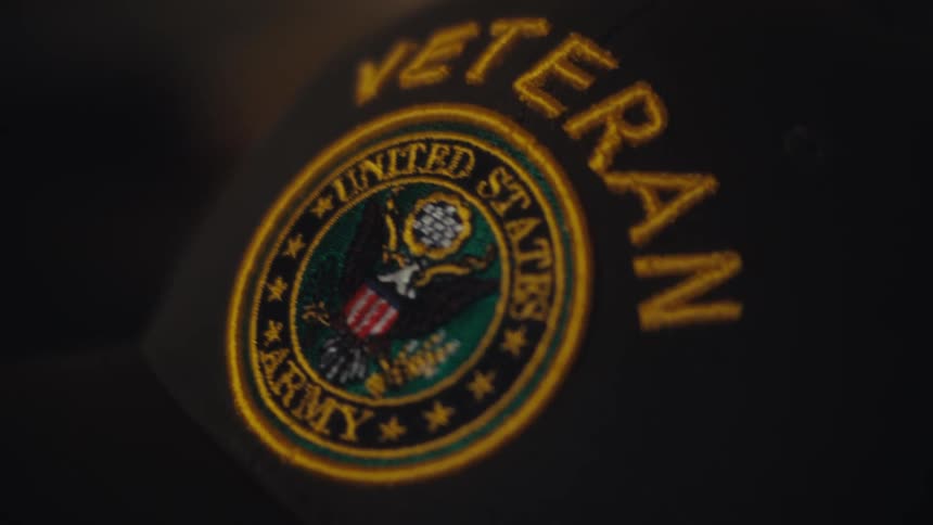 A slow, respectful close-up on the embroidered logo of a United States Army Veteran hat