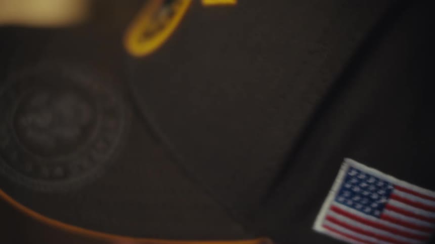 Close-up pan across a U.S. Army Veteran's hat, highlighting the American flag and military insignia