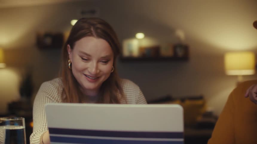 A veteran and his wife happily collaborate on a project using a laptop at their dining table at night