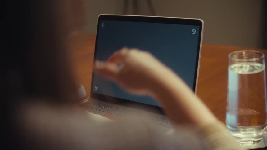 Over-the-shoulder slow zoom out of a person gesturing at a laptop with tracking markers on a wooden desk