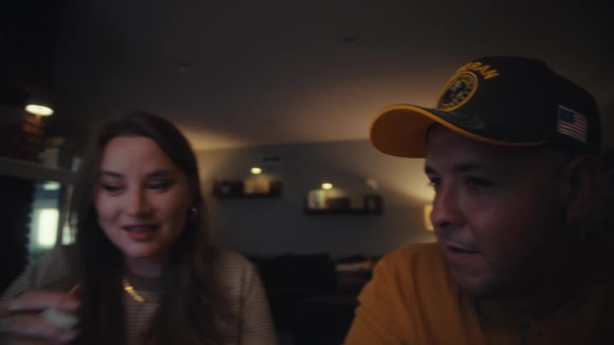 A close-up view of a couple engaging in an animated conversation, their faces illuminated by a screen in their dark living room at night