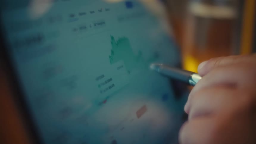 Close-up of a trader's hand with a stylus pointing at a bullish financial graph on a digital tablet