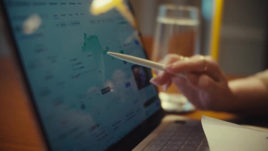 A person uses a stylus to track the price of Ethereum cryptocurrency on a financial chart displayed on a laptop screen