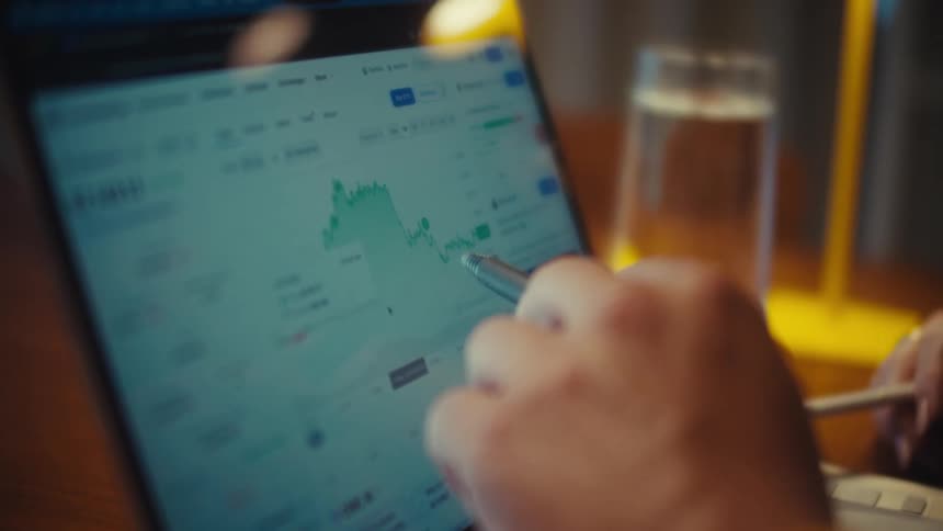 A close-up, soft-focus shot of a person using a stylus to analyze a financial graph on a laptop screen