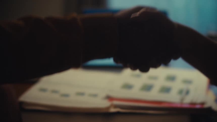 A silhouetted handshake seals a business deal in an office with stock market data displayed on a laptop
