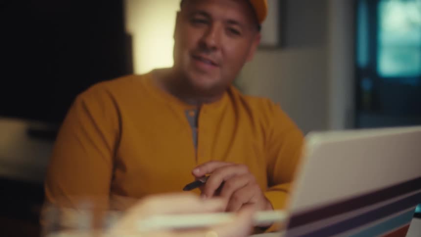 A slow rack focus from a woman's hand holding a stylus over a tablet to a man in a yellow shirt smiling warmly