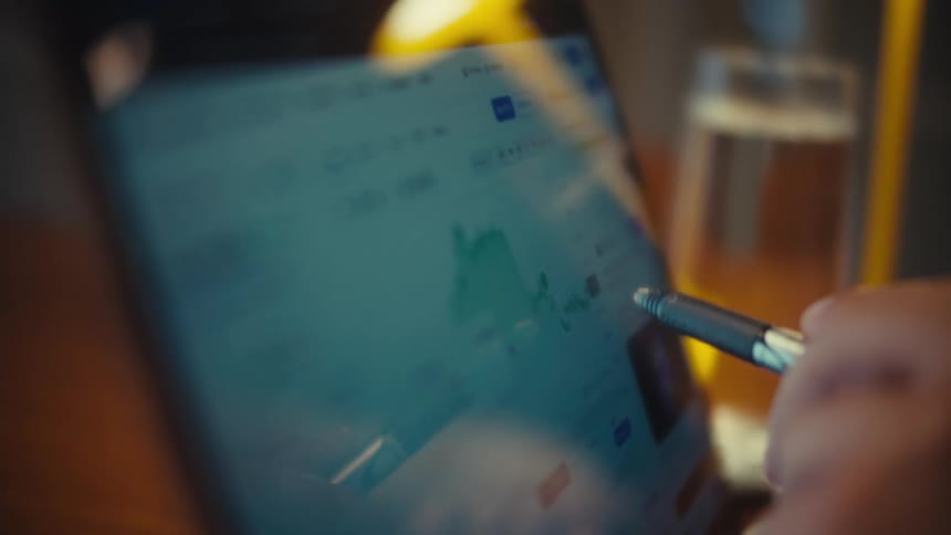 A close-up shot of a hand using a stylus to analyze the Ethereum cryptocurrency chart on a tablet screen