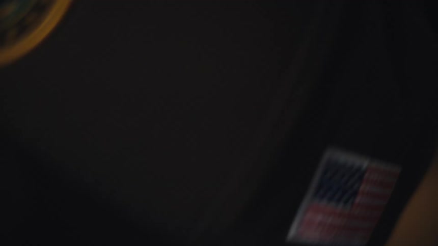 A close-up rack focus shot reveals a veteran's hat with an American flag patch