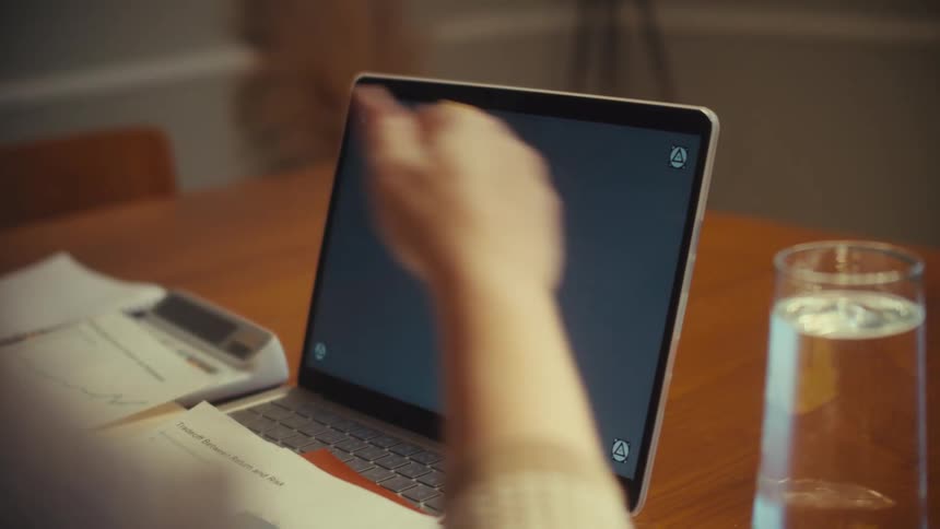 An over-the-shoulder shot of a person working on a laptop with a stylus at their home office desk