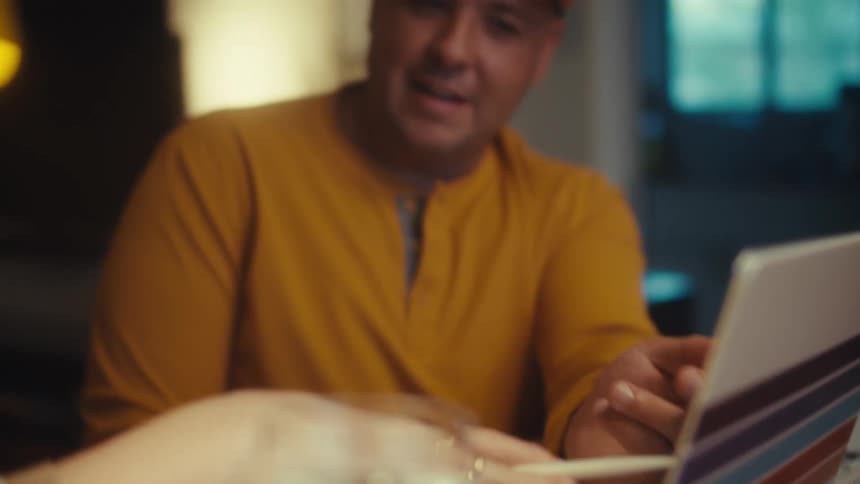 A veteran man smiles and talks with his partner while they work together on their finances at home with a laptop