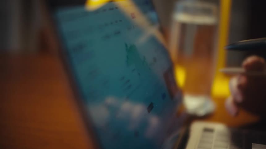 A close-up shot captures hands using a stylus to analyze a fluctuating stock market graph on a laptop screen