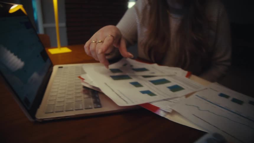 A couple meticulously reviews financial performance charts on paper and a laptop, pointing out key data points