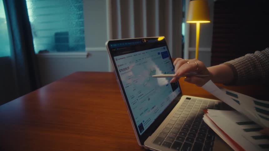 A couple reviews their financial investment portfolio by comparing a printed growth chart with live trading data on their laptop