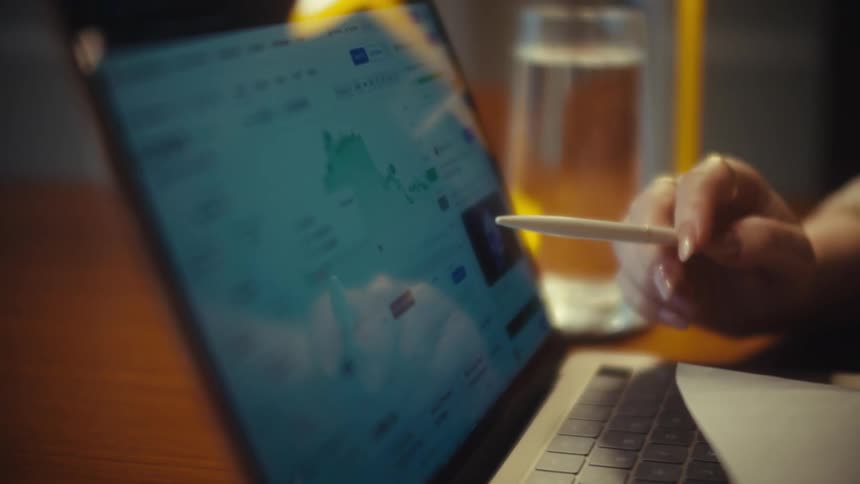 A woman's hand uses a stylus to analyze the performance of Ethereum cryptocurrency on a financial trading website on a laptop