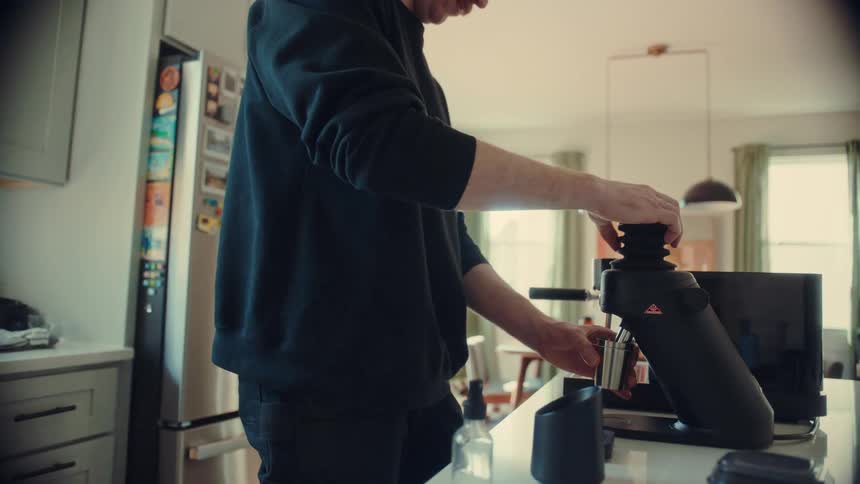A man carefully grinds fresh coffee beans with a specialty grinder in his modern sunlit kitchen