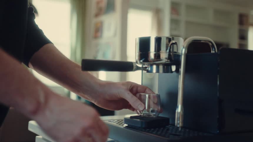 A man carefully locks the portafilter into his espresso machine and places a glass on the scale to prepare a shot