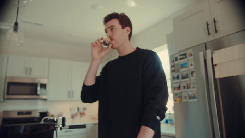 A young man with a mustache swirls and enjoys a fresh shot of espresso in his modern kitchen in slow motion