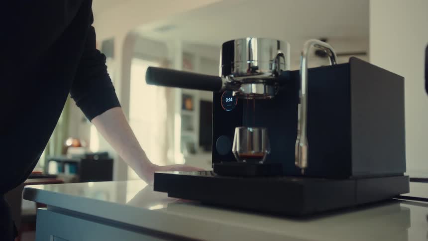A man with a mustache pulls a perfect shot of espresso from a modern machine in a bright, contemporary home kitchen