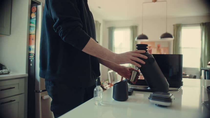A man meticulously grinds fresh coffee beans with a single-dose grinder and prepares a portafilter for an espresso shot in his bright, modern kitchen