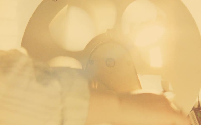 A close-up shot of a hand operating a vintage manual film editing machine with a warm light flare