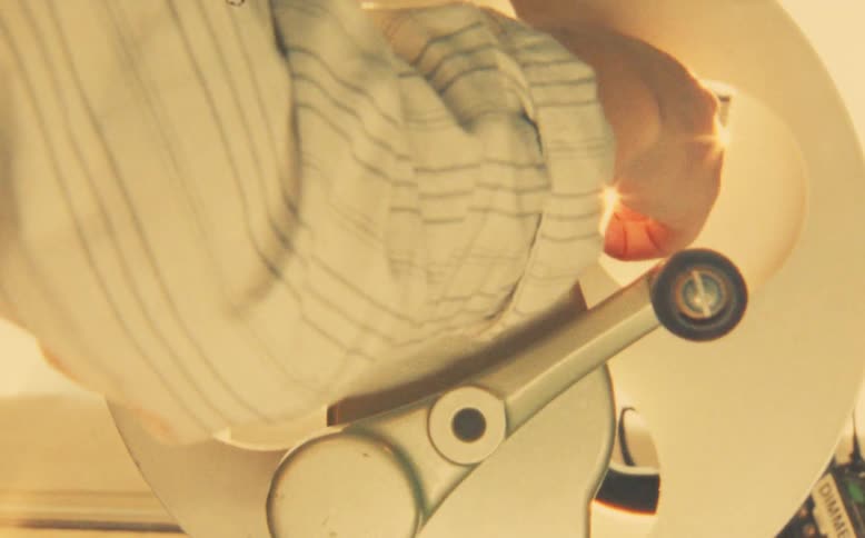 A close-up shot shows a hand turning the crank of a vintage film reel rewinder, creating a nostalgic, warm, and hazy atmosphere
