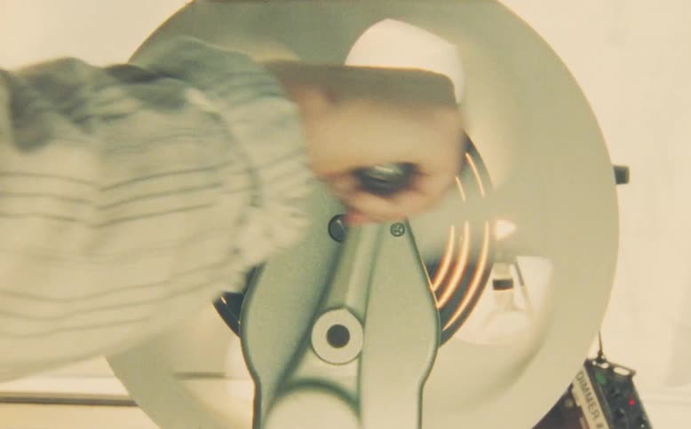 A hand continuously cranks a vintage film reel rewinder, creating a nostalgic and smoky atmosphere