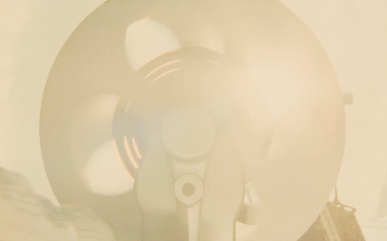 A film editor's hand rapidly rewinds a vintage film reel, with a bright light creating a nostalgic lens flare