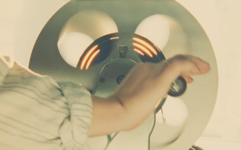 A close-up shot of a hand manually rewinding a film reel on a vintage editing machine