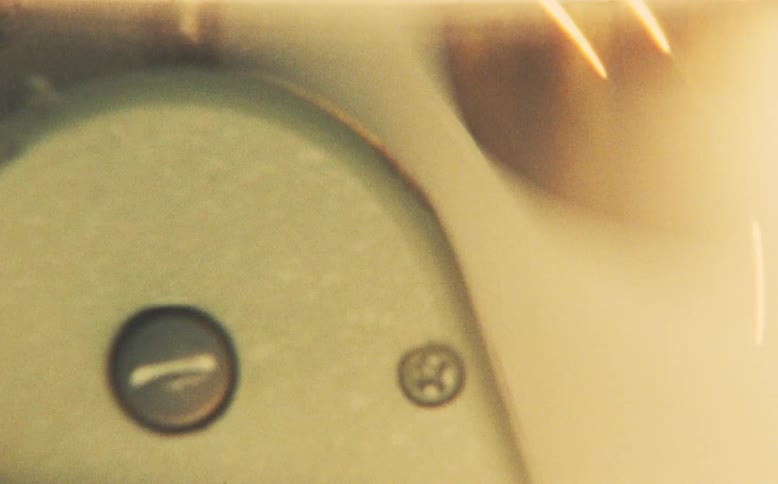 A hand manually operates a vintage film rewinder, causing the reel to spin rapidly under a warm, hazy light