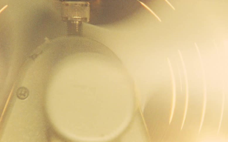 Extreme close-up on the motor of a vintage electric fan as it oscillates and its blades spin in a warm, hazy room