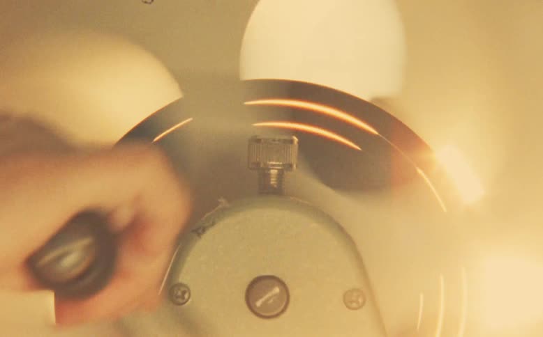 A hand adjusts the oscillation of a spinning vintage fan in a warm, retro-styled close-up shot