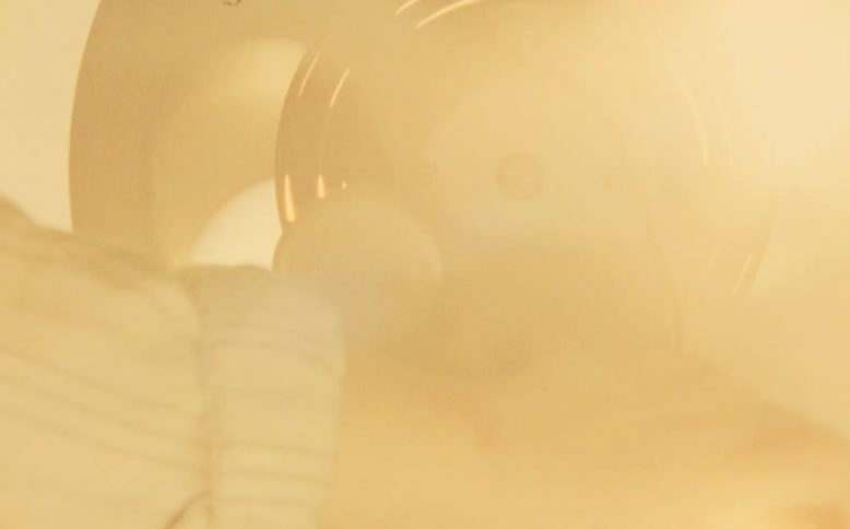 A person's hand cranks a vintage film rewinder, rapidly spinning a reel of movie film in a warm, glowing light