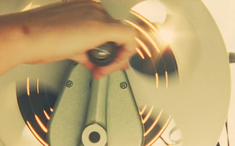 Operating an old-fashioned hand-cranked device, its spinning blades catching the light in a warm, nostalgic close-up
