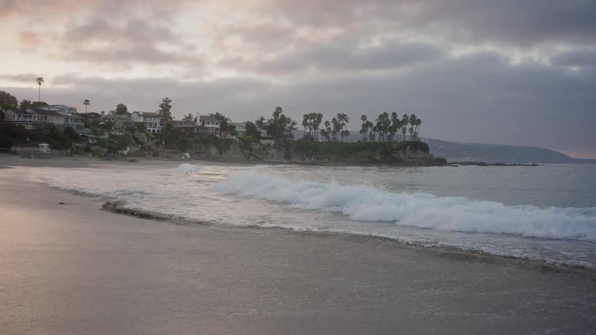 Peaceful slow-motion shot of waves gently washing up on the shore of a California beach during a cloudy sunrise