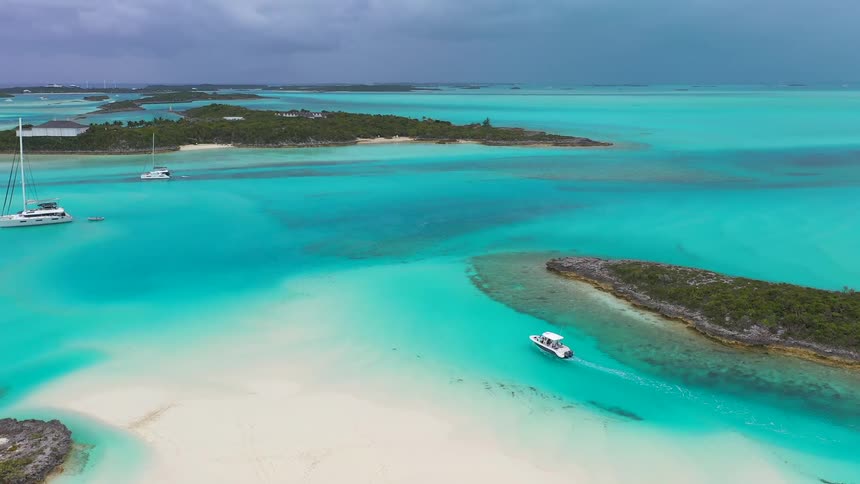 A motorboat cruises through a channel of brilliant turquoise water between tropical islands and white sandbars under a dramatic stormy sky