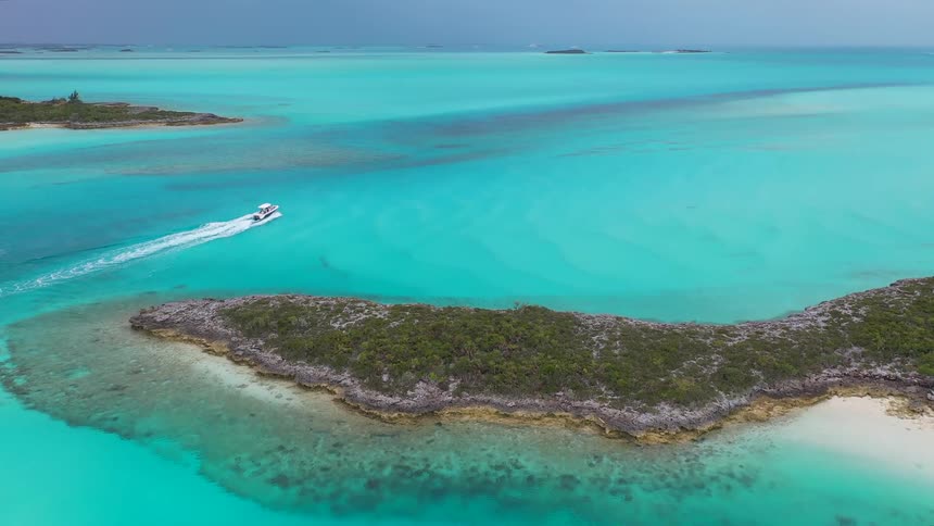 A stunning aerial view shows a motorboat cruising through the brilliant turquoise waters of a tropical archipelago