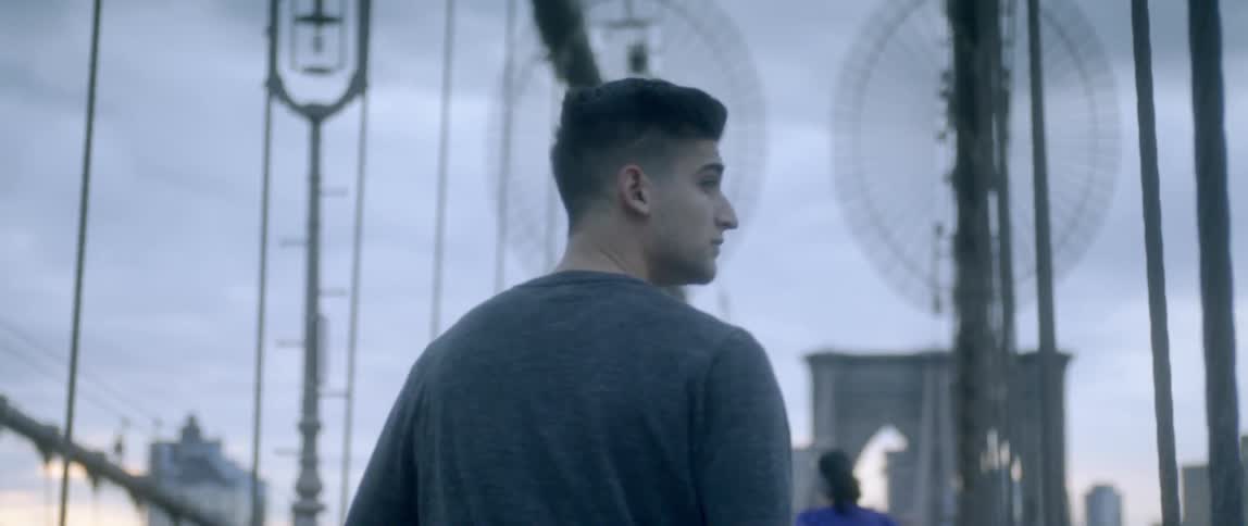 A man in a gray shirt walks along a bridge outside