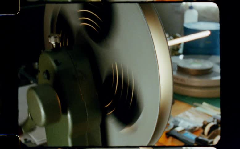 A vintage manual film rewinder rapidly spins a film reel as a hand turns the crank in a classic 8mm film style