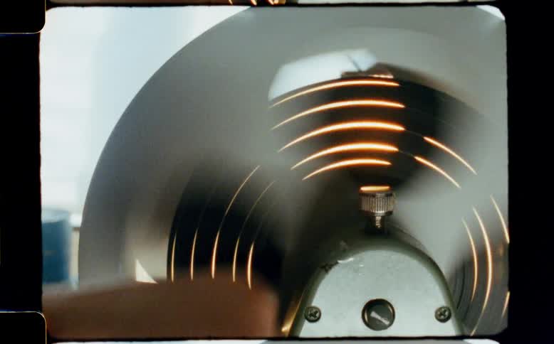 A spinning reel from a vintage tape recorder reflects golden light, captured on authentic 8mm film
