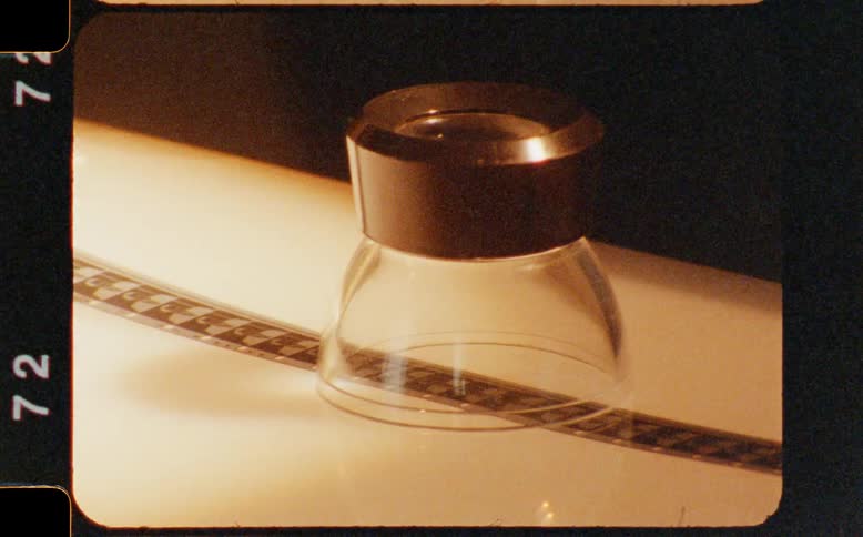 A vintage-style shot of a film editor's loupe on a strip of film as light sweeps across the scene