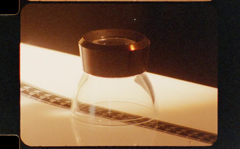 A vintage-style shot of a film editor's loupe and a strip of film on a lightbox, framed by sprocket holes